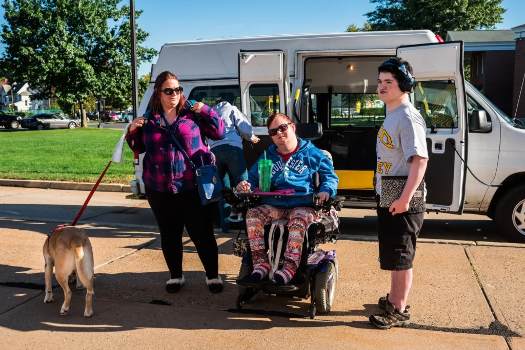 Students and support staff with a service dog gathered outdoors near a campus van for Professionals.